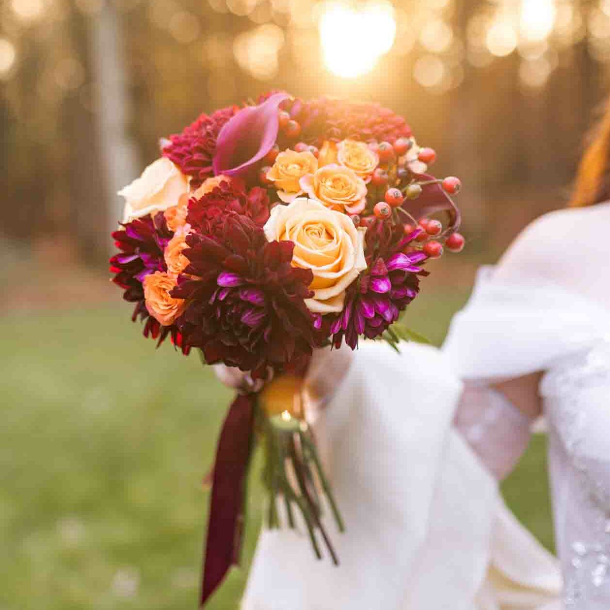 Photographe mariage au domaine de la Roche Couloir avec le bouquet de la mariée. Ambiance automnal avec des teintes d'orange, bordeaux et violet, capturé dans la lumière dorée du coucher de soleil.