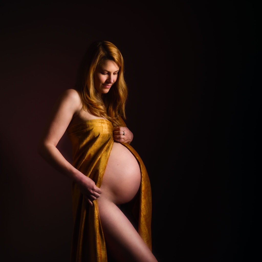Photo de grossesse artistique avec drapé doré, lumière picturale, séance grossesse œuvre d'art en studio à Rueil-Malmaison.