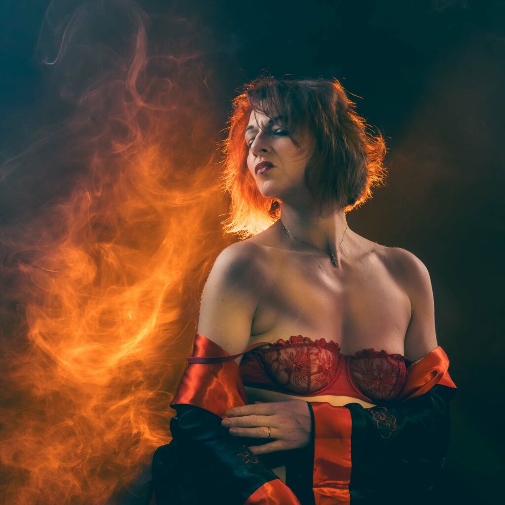 Portrait boudoir élégant, femme aux cheveux cuivrés et épaules nues dans une fumée ambrée, séance intimiste en studio.