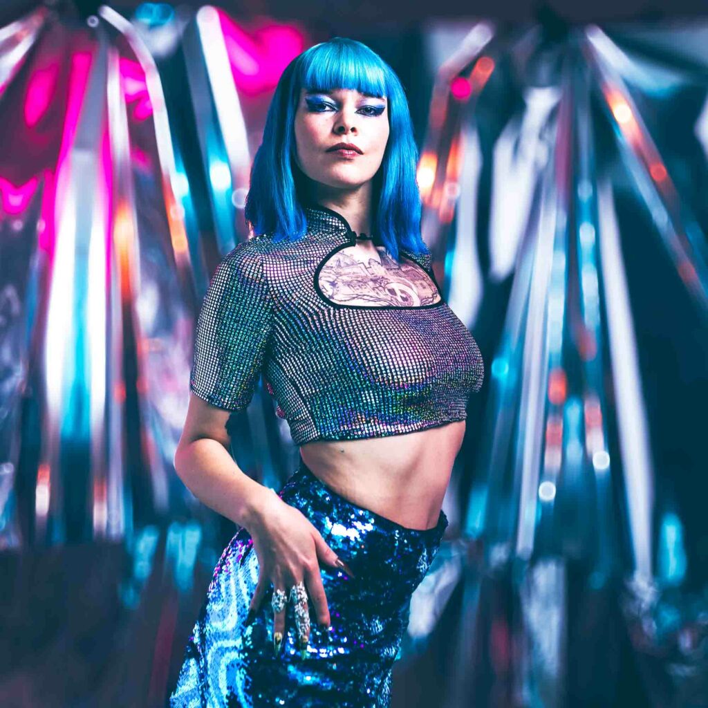 Portrait CyberWave années 80, femme aux cheveux bleus en top métallique devant un décor chromé, studio Rueil-Malmaison.