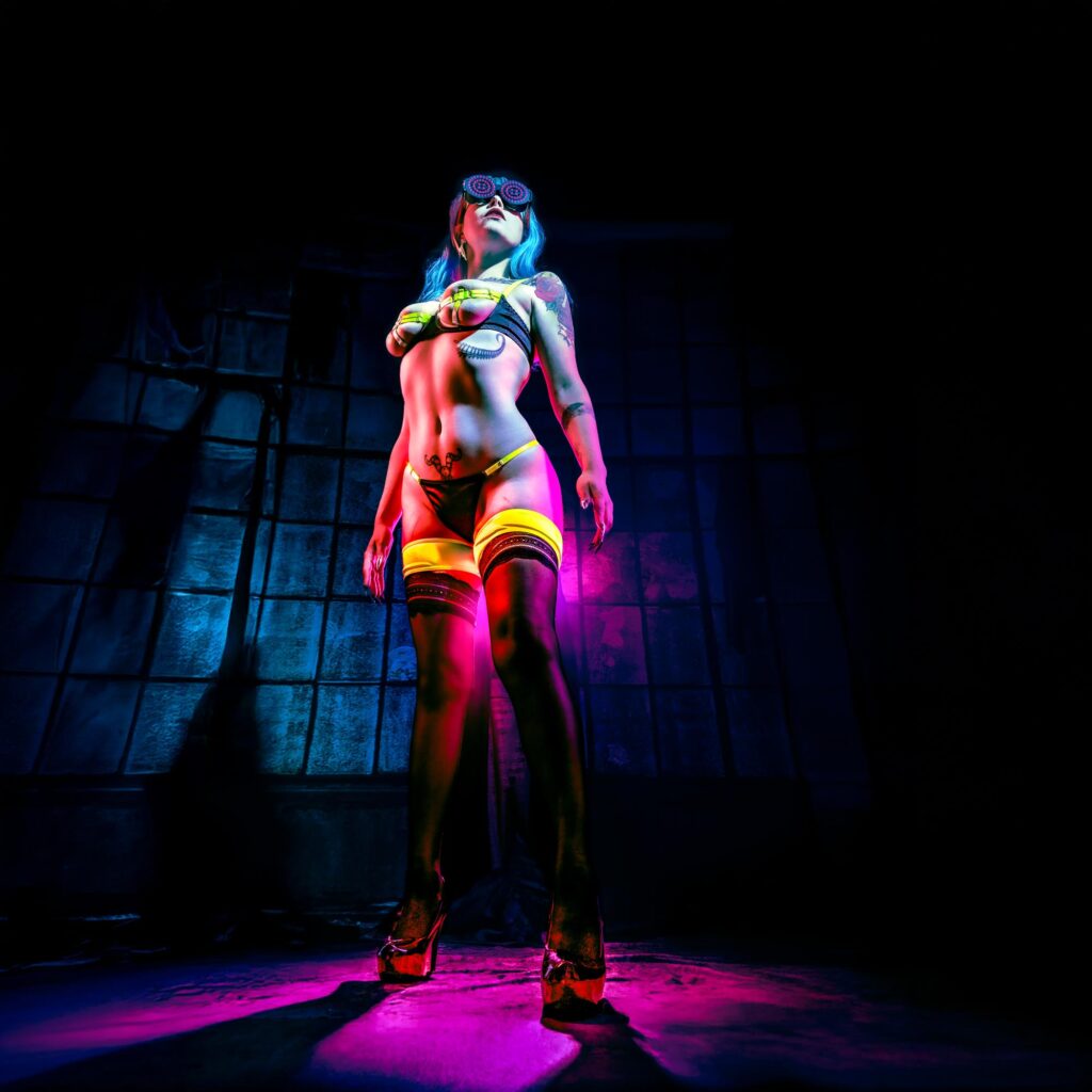 Portrait en pied en contre-plongée, femme aux lunettes LED futuristes devant une fenêtre d'usine bleue, style cyberpunk.
