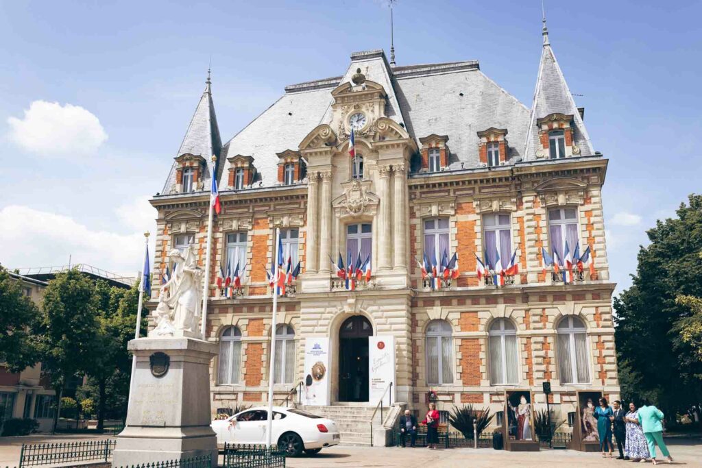 Façade pavoisée de l’hôtel de ville de Rueil-Malmaison, voiture des mariés garée devant et invités sur le parvis
