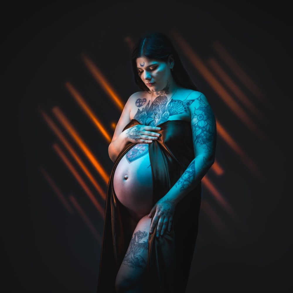 Photo de grossesse artistique en studio à Rueil-Malmaison, future maman tatouée en lumière colorée